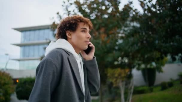 屋外でスマートフォンを話す穏やかなヒップスター 秋の通りを歩く電話をする若い男 自信ある若者が話しかけている カジュアルなティーンは友人会議に移動します 都市ライフスタイルのコンセプト — ストック動画