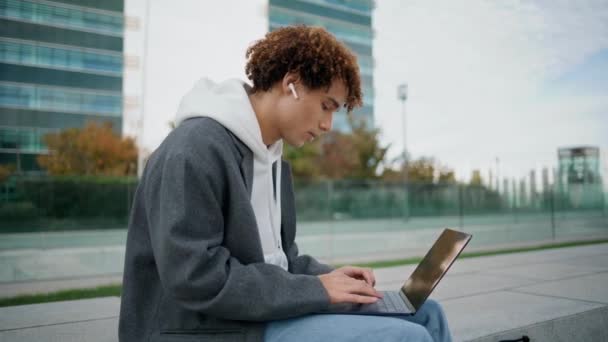 Krullende Tiener Typt Laptop Straat Close Jongeman Luistert Muziek Met — Stockvideo