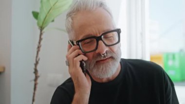 Sakallı, yaşlı, cep telefonlu, yakın çekim. Gülümseyen kreatif yönetici hücre hücre işleri hakkında konuşuyor. Başarılı acımasız iş adamı burun piercing 'i takıyor. Yakışıklı, olgun bir adam..
