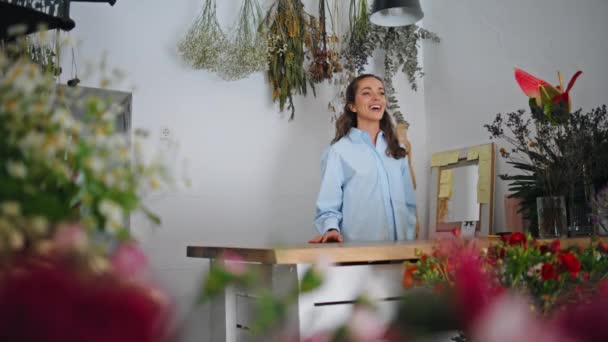 店内でポジティブなフラワーショップのデコレータトーク 美しい女性花屋の所有者は花の背景で微笑みます 売り手を笑う起業家は 植物店でポジティブなエネルギーを話します 現代のビジネスマンコンセプト — ストック動画