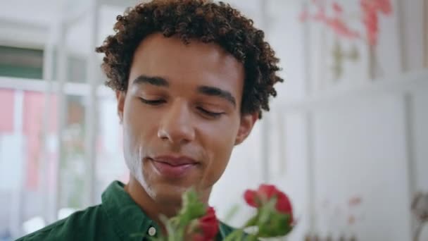 美しいアフリカの男は花屋の閉店でスプレーバラを楽しんでいます 美しいカーリーヘアの男は植物店の春の花束の匂いを嗅ぐ ハンサムな笑顔のクライアントは花の構成を購入します 美しさ コンセプト — ストック動画