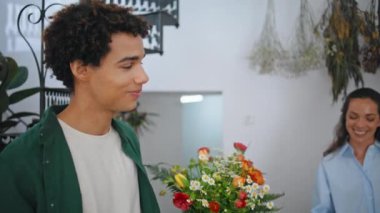 Gülümseyen müşteri çiçekçiden çiçek almaktan hoşlanıyor. Mutlu Afrikalı adam çiçekçi dükkanından çıkarken yaklaş. Yakışıklı kahverengi tenli yetişkin, güle güle de. Butikte kameraya bak. İletişim konsepti.