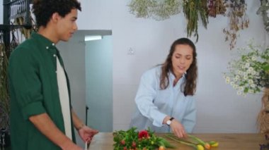 Afrikalı müşteri çiçekçiden çiçek alır. Çiçekçi kız yaz tatili mağazasında bahar buketinde çalışıyor. Genç ve güzel bir kadın çiçek dizaynı ile çiçek kompozisyonu hazırlıyor. Sanatsal kavram.