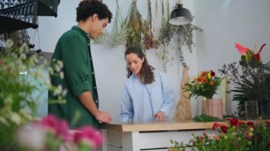 Modern çiçekçiden çiçek almak için kredi kartı kullanan bir alıcı. Yakından siyah saçlı bir adam kasadaki çiçekçiye ücretsiz ödeme yapıyor. Dükkan sahibi kadın butikte çalışıyor. Ödeme faturası kavramı.