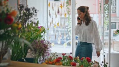 Çiçekçinin işyerindeki çiçekçi sohbet cep telefonu. Meşgul bir kadın, çiçekçide müşteri desteği için akıllı telefon kullanıyor. Kapatın. Olumlu bir iş adamı internet üzerinden yardım istemcisini tartışır. İletişim konsepti