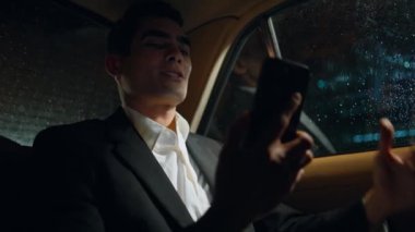 Neşeli iş adamı iş arabasındaki cep telefonundan video görüşmesi yapıyor. Happy yönetici modern araçta motive edici video kaydediyor. Neşeli adam otomobildeki sanal mesajla iyi haberler veriyor.