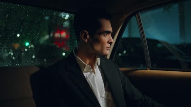 漂亮的商人在夜间特写时看着车窗 一个严肃的男人坐在后座上 和私人司机一起驾驶现代汽车 成功优雅的经理凝视着雨夜城 奢华之旅 — 图库视频影像