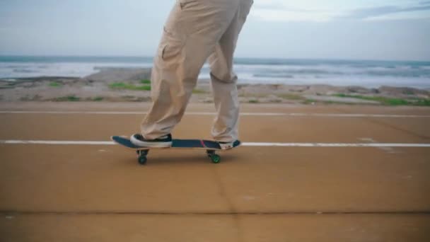エンバンクメント海道のスケートボードに乗っている男の脚が近くにあります 未知のスケーターの男は 遅い動きで海岸でロングボードのトリックを訓練します アクティブスケートボーダーフィートバランススケートボードジャンプ — ストック動画