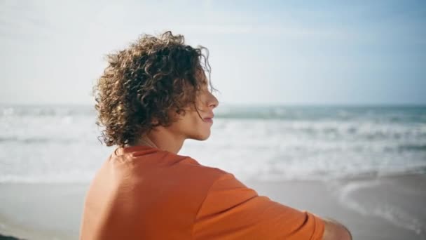 Młody Spokojny Mężczyzna Siedzący Oceanicznej Plaży Przy Ciepłym Letnim Świetle — Wideo stockowe