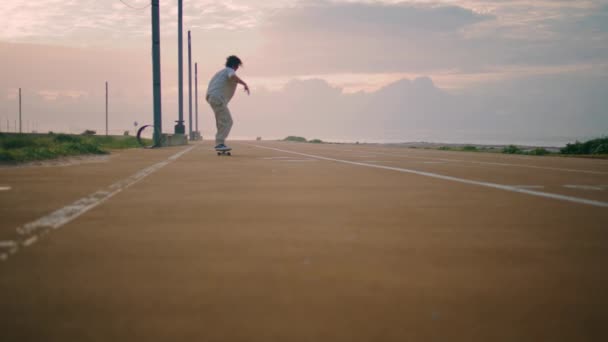 日没の海の背景にあるスタイリッシュなヒップスタージャンプスケートボード アクティブなスケーターボーイは 夏のエンバンクメントに乗るスピードを楽しんでいます 夜のトレッドミルでトリックを作るスケートボードのバランスをとる若いスポーツマン — ストック動画