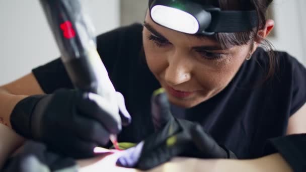 严肃的艺术家使用纹身机在沙龙肖像 Latex黑色手套纹身师在家里工作室工作的特写镜头 焦点女性穿着手电筒在客户身上创造图片 艺术概念 — 图库视频影像