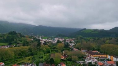 Orman kırsalında bulutlu bir günde doğa havası. Gökgürültüsü bulutlarının altında panoramik resimli dağ mimarisi manzarası. Yeşil ormanlık tepelere konmuş rahat evler. Taze vadi köyü ağır çekim