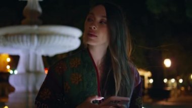 Akıllı telefonları olan bir kadın şehir çeşmesinin yanında toplanmayı bekliyor. Gece yakın plan. Elinde cep telefonu olan güzel bir kız şehrin karanlık bölgelerine bakıyor. Harika bir bayan cep telefonuyla toplantı düzenliyor.