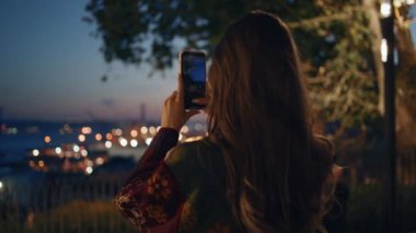 Akıllı telefondan gece çekimleri yapan bir kadın gözlem güvertesini kapatıyor. Genç kız blog yazarının cep telefonuyla panoramik fotoğraf çekilen şehir ışıkları görüntüsü. Bayan turist kasaba fotoğrafı çekiyor..