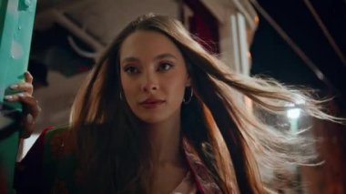 Alacakaranlık akşamında poz veren modaya uygun bir model. Rüzgâr tarafından savrulan uzun saçlı güzel bir genç kadının portresi. Muhteşem kendine güvenen kız yaz gecesi şehir binasında dikiliyor..