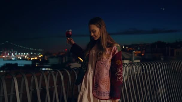 一个无忧无虑的女人 带着鸡尾酒在街边散步 看起来像是夜晚的都市风景 时尚的女孩喝酒 享受周末镇上的娱乐活动 在户外玩乐的松懈女士 — 图库视频影像