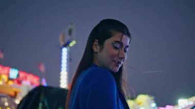Çekici kız Aydınlanmış Ay Parkı 'nda akşamın tadını çıkarıyor. Karanlık gökyüzüne yakın poz veren güzel bir model. Neşeli, gülümseyen bir kadın eğlence fuarı neon atlıkarıncasını hafta sonu gecesi dinlendiriyor. Romantik pozitif kadın konsepti
