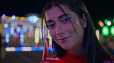 Lunaparkta lolipop tutan güzel bir kız. Romantik kadın kamerası lunaparktaki yaz akşamının tadını çıkarıyor. Güzel gülümseyen genç dinlenme festivali aydınlatılmış bokeh ışıklarında.