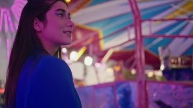 Gülümseyen kız eğlence parkının yakın çekimlerinde iyi eğlenceler. Heyecanlı kadın dinlenme eğlence fuarı neon dönme dolap atlıkarıncanın tadını çıkarın. Neşeli model kamera görüntüsü. Hafta sonu eğlence konsepti