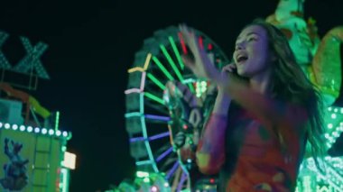 Akıllı telefondan konuşan bir kadın arkadaşlarına el sallıyor. Aydınlatılmış Lunapark 'ta hücrede konuşan neşeli kız buluşması. Randevudayken gülümseyen genç bir erkek arkadaş. Hafta sonu eğlence konsepti 