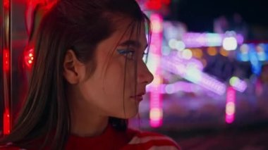 Çekici kız eğlence fuarına yakın çekim. Neon Lunaparkında bekleyen mutsuz, üzgün bir kadın. Moda makyajlı, üzgün, muhteşem bir model. Aydınlanmış fuarda romantik bir randevuda düşünceli bir genç..