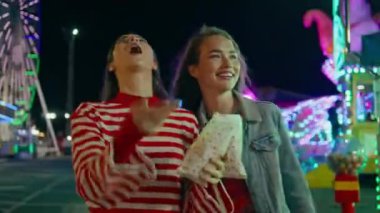 Tatilde yürüyen mutlu kızlar festivali. Aydınlatılmış lunaparkta elinde abur cubur tutan komik arkadaşlar patlamış mısır kusuyor. Neşeli gülümseyen gençler şehir karnaval sokağına gitmekten zevk alıyorlar..
