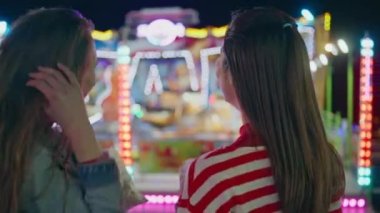 Yakından eğlenceli arkadaşlar renkli lunaparkları dinlendiriyorlar. İki kız festival arka camında yanıp sönen atlıkarıncayı seyrediyor. Şehir karnavalındaki rahat, neşeli gençler. Hafta sonu eğlence eğlencesi