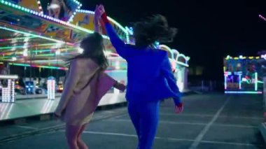 Lunapark caddesinde dans eden neşeli kızlar. Mutlu iki arkadaş renkli aydınlatılmış atlıkarıncada hafta sonunun tadını çıkarıyor. Gülümseyen mutlu sevgili çifti lunapark gecesinde birlikte eğleniyor.