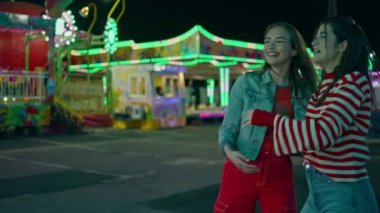 Mutlu kızlar lunapark karnavalına sarılıyor. Neşeli arkadaşlar lunaparkta eğleniyorlar oyun makinesinde yüksek puanları kutluyorlar. Festivalde yaz tatilinin keyfini kucaklayan neşeli gençler.