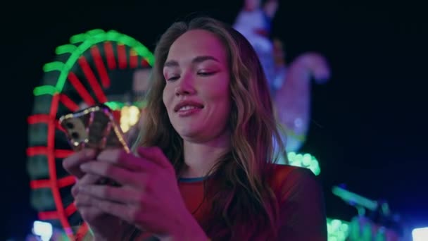 照らされたフェリスの車輪でスマートフォンをタイプするクローズアップガール ハッピーモデルは 夜の都市フェスティバルでソーシャルメディアを使用してオンラインでメッセージを送信します アミューズメントパークで友達を待っている魅力的な女性チャット — ストック動画