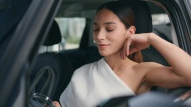 Kendine güvenen bir bayan, arabanın ön koltuğunda oturmuş akıllı telefon ekranına yakından gülümseyerek bakıyor. Başarılı bir iş kadını. Pahalı arabaların içinde telefonla mesajlaşıyor. Genç kız sürücü park yerinde dinleniyor..