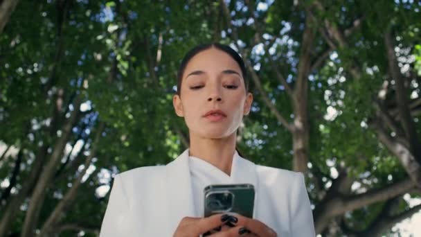 緑の公園の木の近くに立っている携帯電話を見ている失望した女性ボス 外でスマートフォンに悪いメッセージを受け取るエレガントな豪華なビジネスマン 銀行ローン通知を読んでいる心配な女性 — ストック動画