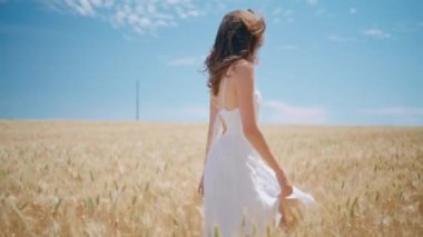 Güneşli buğday tarlalarında tek başına yürüyen ışıldayan kadın. Yaz tarlasında gülümseyen neşeli kız. Mutlu kadın güzel kırsal doğayı döndürüyor. Olumlu genç model ülke manzarasını keşfediyor