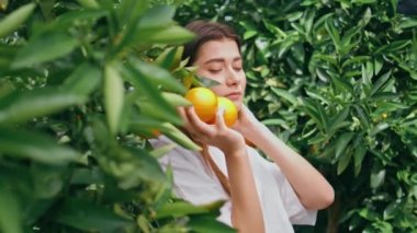 Yeşil doğa portresine portakal poz veren nazik bir kadın. Botanik bahçesinde kameraya bakan şehvetli, muhteşem kız. Mutlu, narin esmer, yazın tadını çıkarıyor. Turunçgil tarlalarında dinleniyor. 