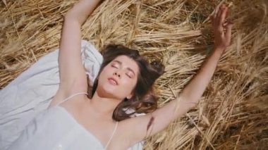 Güneşin tadını çıkaran şehvetli bir kadın buğday dikenlerinin üzerinde uzanıyor. Yaz otlağı manzarasında el ele oynayan güzel bir kız. Neşeli, rahat bir bayan kollarını uzatıyor güneşli kırsalda dinleniyor.