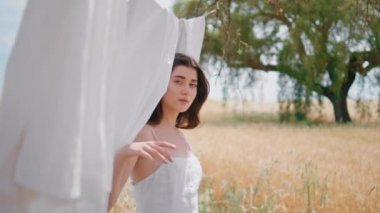 Kırsal kesimdeki portrede çamaşır asarken ortaya çıkan genç bayan. Hassas, şehvetli esmer, kameraya baştan çıkarıcı bir şekilde yakından bakıyor. Göz kamaştırıcı kadın ellere dokunuyor keten ipler güneş ışığında gözleri kapanıyor