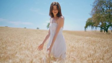Rahat bir kadın, gün ışığında çiftlikte geziniyor. Gülümseyen bayan sabah çayırında doğa yürüyüşünün tadını çıkarıyor. Tarım hasadında buğday saplarına dokunan dingin, güzel bir el modeli. Basit zevkler. 