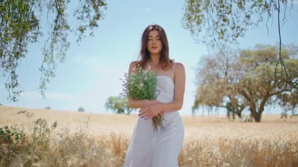 一个浪漫的女人拿着野花束 看着花园的相机 泰然自若的女孩 拿着迷迭香花在麦田里散步 布鲁内特的头发在农村自然直 农村生活 — 图库视频影像