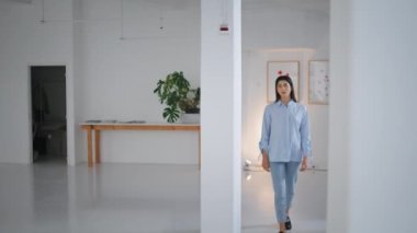 Başarılı bir iş kadını poz veriyor. Kendine güvenen esmer kadın, beyaz duvara yaslanmış, sıradan kıyafetli kameraya bakıyor. Çağdaş sanat galerisinde çalışan gururlu genç model. İş sahibi kavramı