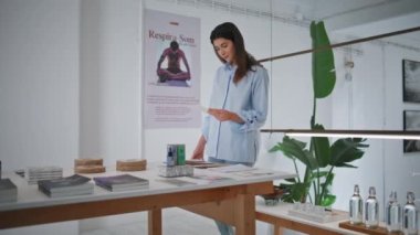 Kaplıca lobisinde bekleyen bir kadın eşyaları kontrol ediyor. Yoga merkezini ziyaret eden düşünceli bir müşteri indirim bilgileri okuyor. Mağaza masasından bir şeyler seçen çekici esmer kız. Butik müşteri konsepti.