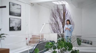 Modern ofis salonunda yürüyen bir kadın. Su bardağı tutan başarılı iş kadını boş odada mola veriyor. Kameraya bakan barışçıl gülümseyen menajer sanat galerisinde tek başına vakit geçirmenin tadını çıkarıyor. Gururlu iş sahibi