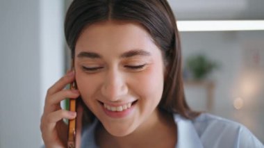 Evde cep telefonuyla konuşan mutlu bir kız. Çekici esmer bakışlı kamera kapanış konuşmasını kapatıyor. Neşeli gülümseyen kadın akıllı telefon konuşmasından hoşlanıyor. İş kadını iş yerinde dinleniyor..