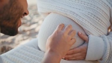 Sevimli koca hamile kadının karnını okşuyor doğmamış bebeği öpüyor. Genç, müstakbel baba kocaman karnını okşuyor, şefkat duyuyor. Tasasız aile çifti hamileliğin tadını çıkarıyor..