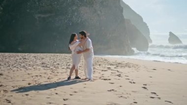 Güzel güneşli sahilde bebek bekleyen çift yaz tatilinin tadını çıkarıyor. Mutlu hamile kadın, sevgili kocasıyla gülümsüyor ve altın deniz kumu üzerinde yürüyor. Romantik aile çocuk bekliyor..