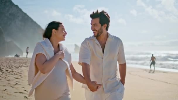 快乐的怀孕家庭手挽手走在美丽的夏季海滨 快乐可爱的夫妻在海滩散步时一起谈笑着 无忧无虑的未来父母享受海滨度假 — 图库视频影像