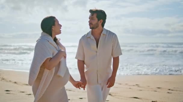 赤ちゃんを期待する海岸を散策するロマンチックなカップル 美しい晴れたビーチを歩く手を握っているケアフリーの妊婦 ハッピーハンサムな夫は海岸で夏休みを楽しんでいる若い妻にキス — ストック動画