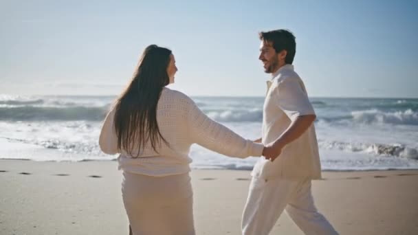 ビーチを散策する愛する配偶者は 近くでハネムーンをお楽しみください ハッピーロマンチックなカップルは 砂の海岸の夏の休日に歩いて抱擁しています 笑顔のひげをした夫は自然に美しい若い妻にキス — ストック動画