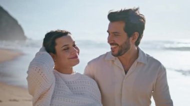 Kaygısız genç eşler güzel güneşli okyanus kıyısında yakın mesafede gezinirler. Kumsalda yürüyen mutlu romantik çift aşk mutluluğunu hissediyor. Gülümseyen koca kıyıda sevimli karısını öpüyor.