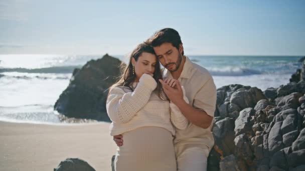 在家庭度假特写的时候 和平的期待着的父母们喜欢站在阳光灿烂的海滨站在一起 有爱心的丈夫依偎在海滩悬崖峭壁上 温柔地拥抱心爱的怀孕妻子 幸福的配偶拥抱 — 图库视频影像