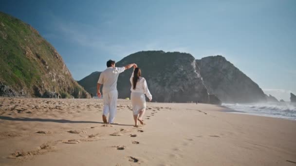 妊娠中の愛好家は 夏休みを一緒に楽しむビーチサンドを散策しています ベアフット 幸せなカップル 足跡を残して海岸を踏みます 愛する夫 美しい 赤ちゃん — ストック動画